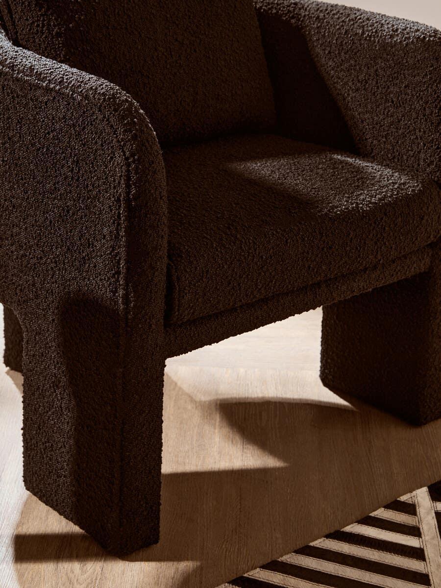 Brown textured armchair with rounded arms and plush seat on wooden floor beside geometric rug