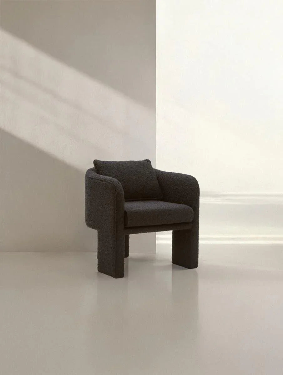 Modern dark fabric armchair with cushioned seat in minimalist room with natural light