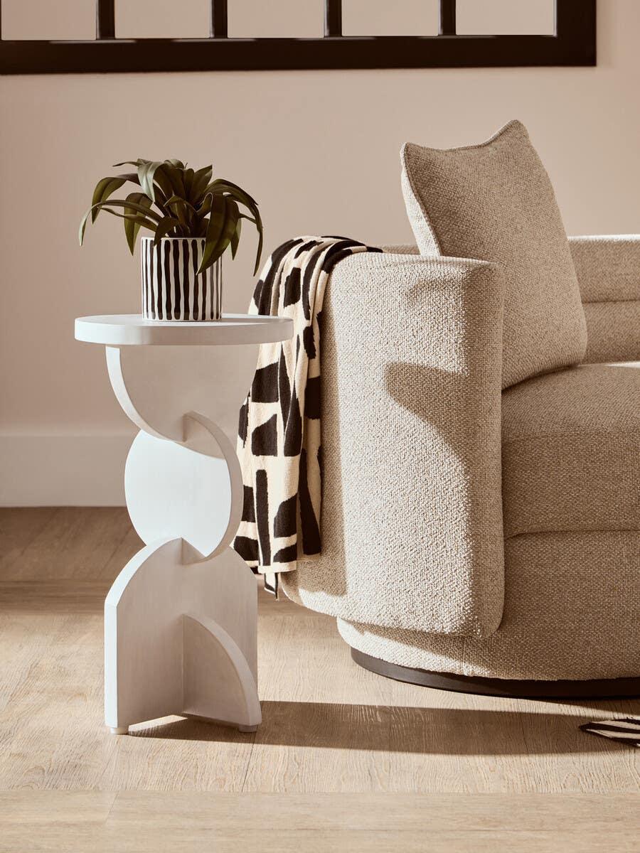 Modern beige sofa with textured upholstery beside sculpted white side table and potted plant