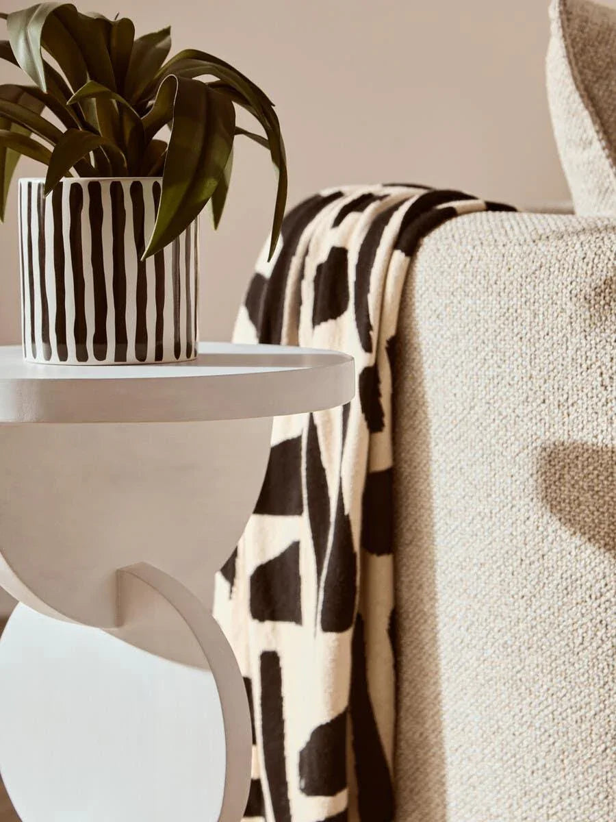 Modern side table with potted plant beside textured beige sofa and patterned throw blanket