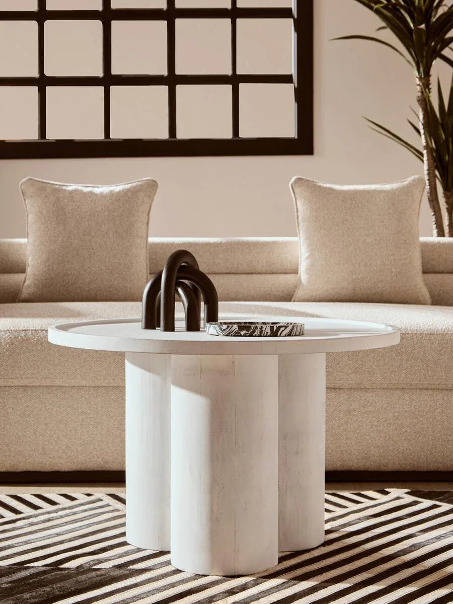 Round white coffee table with sculpted legs in modern living room with beige sofa