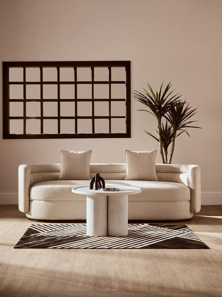 Modern cream sofa with curved arms, two cushions, round coffee table, and striped rug