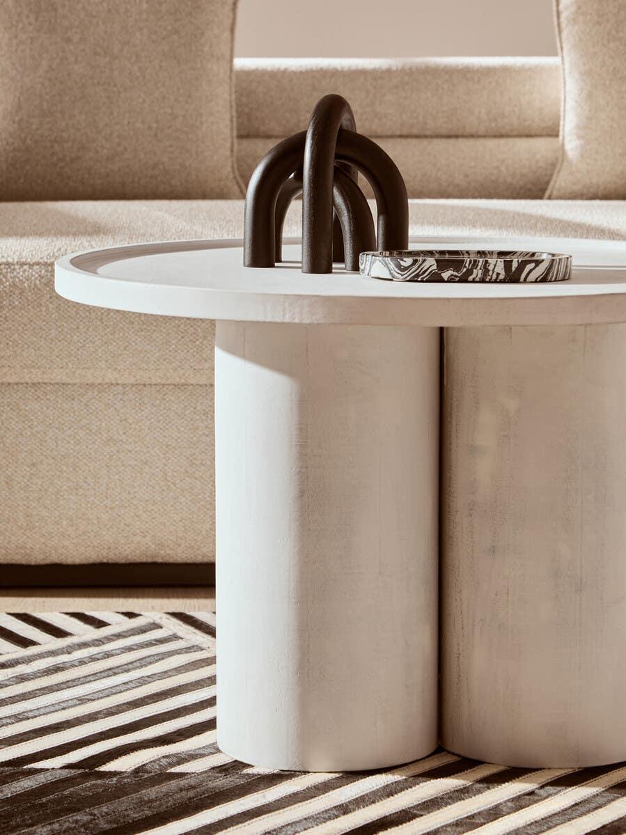 Round modern coffee table with sculptural decor and marble tray on striped rug