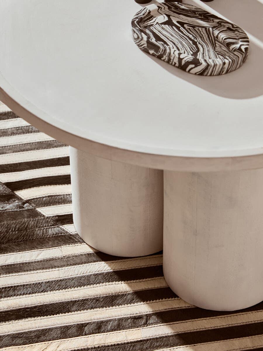 Round white coffee table with cylindrical legs on striped rug, modern living room decor