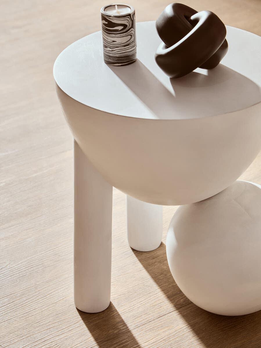 White modern side table with candle and sculptural decor on wooden floor