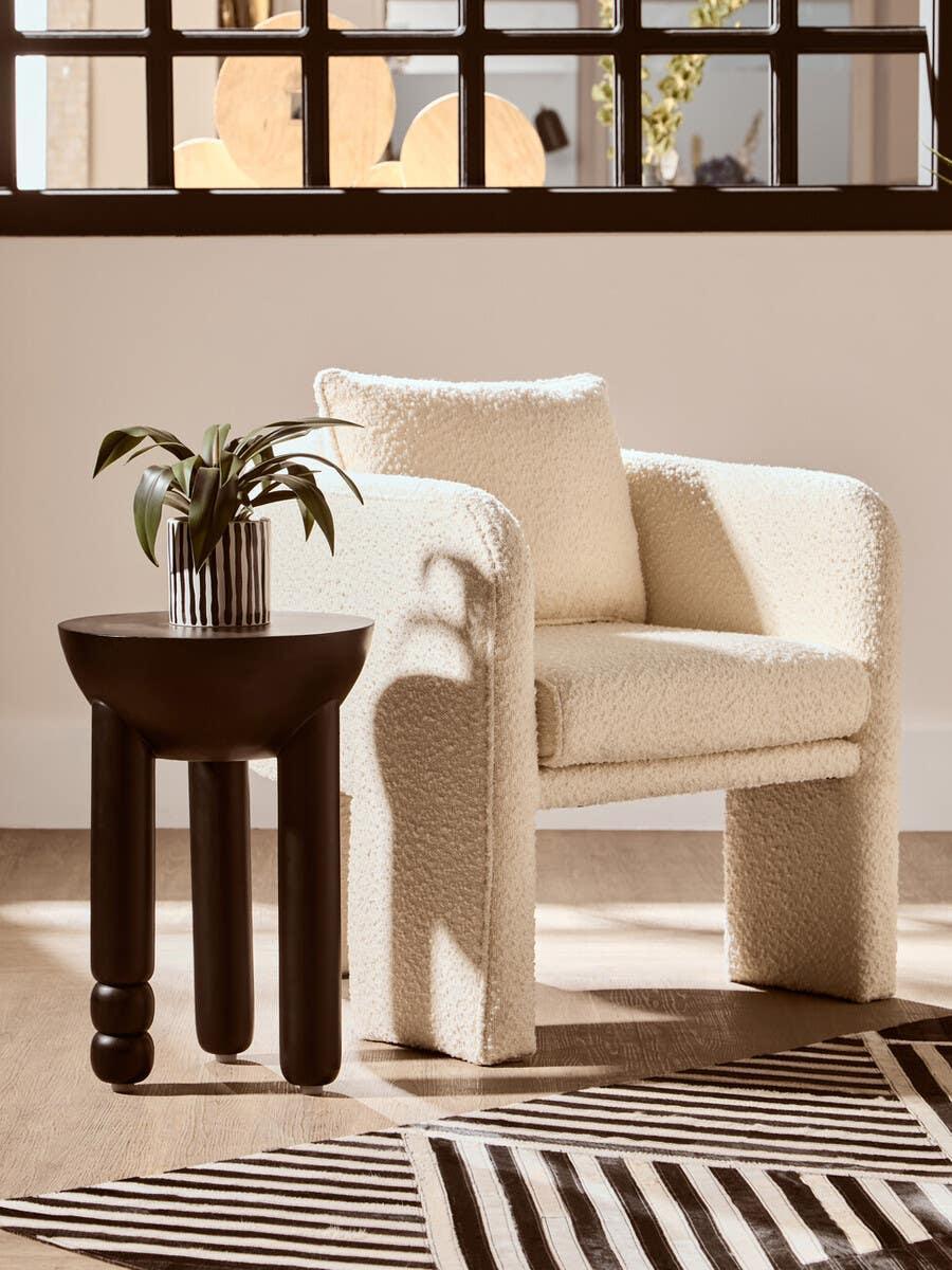 Cream boucle accent chair with cushion beside modern black side table and striped rug