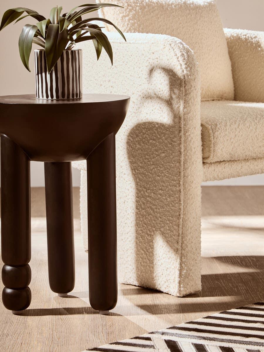 Cream boucle armchair beside a dark wood side table with striped plant pot and rug