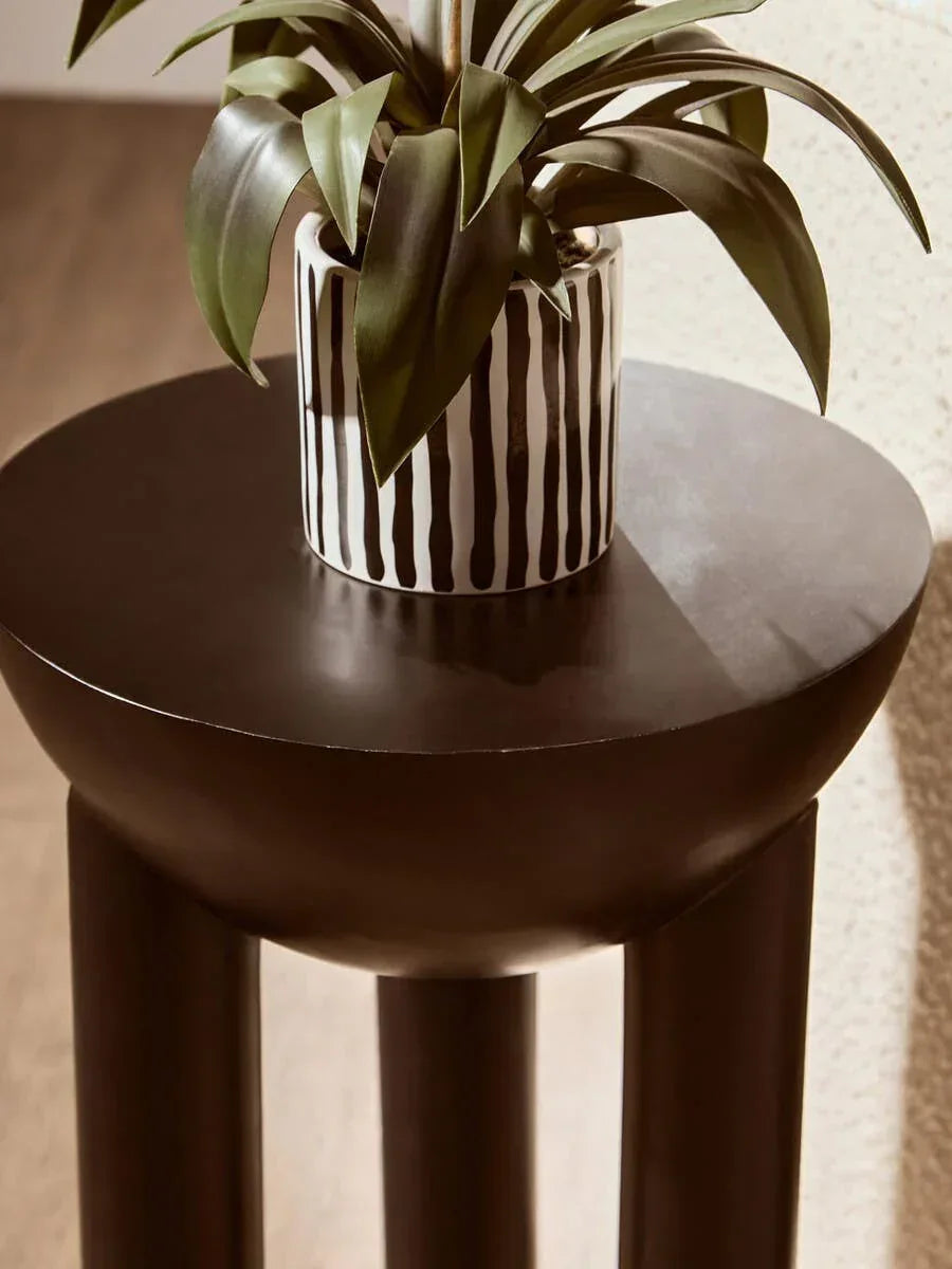 Round dark brown side table with decorative plant in striped ceramic pot