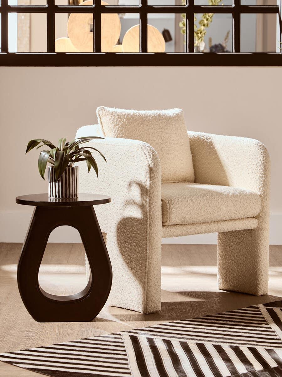Cream boucle armchair with cushion beside black side table and stripe rug in living room