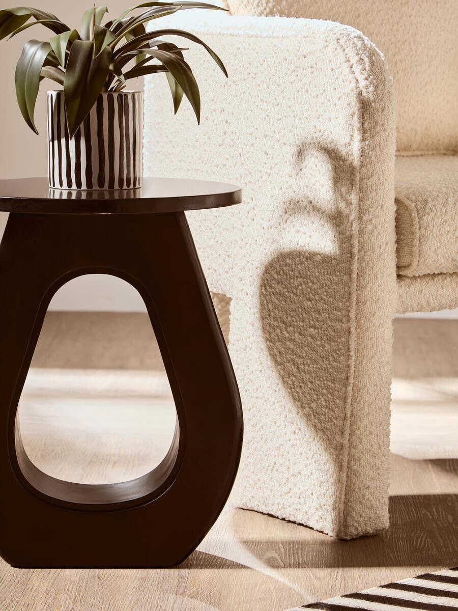 Cream boucle armchair next to dark wood side table with potted plant on hardwood floor