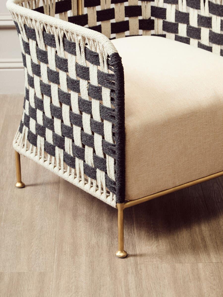 Woven accent chair with black and cream rope sides, beige cushion, and gold metal legs
