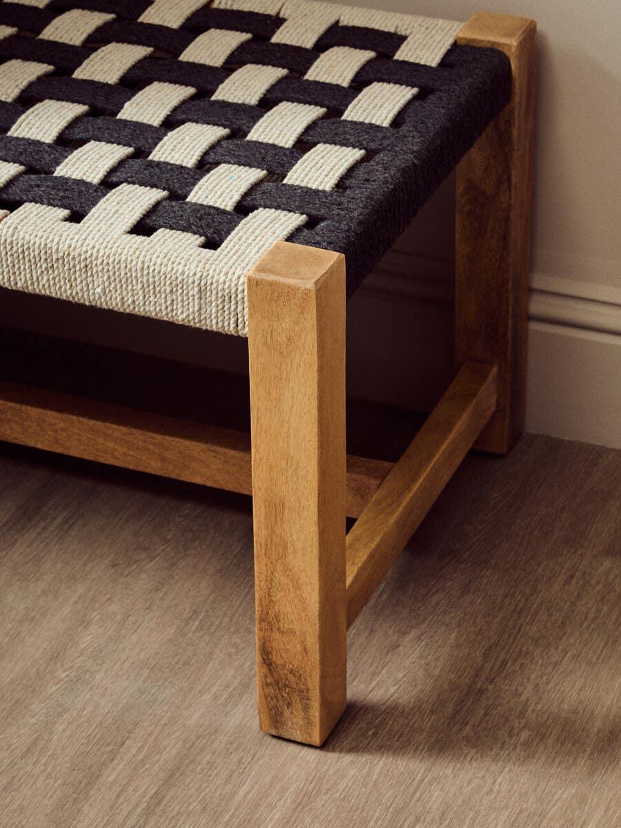 Wooden bench with black and cream woven fabric seat on laminate flooring