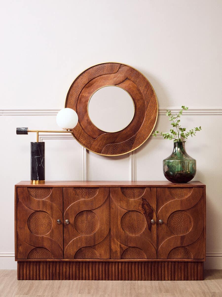 Wooden sideboard with geometric pattern, round mirror, lamp, and vase on top