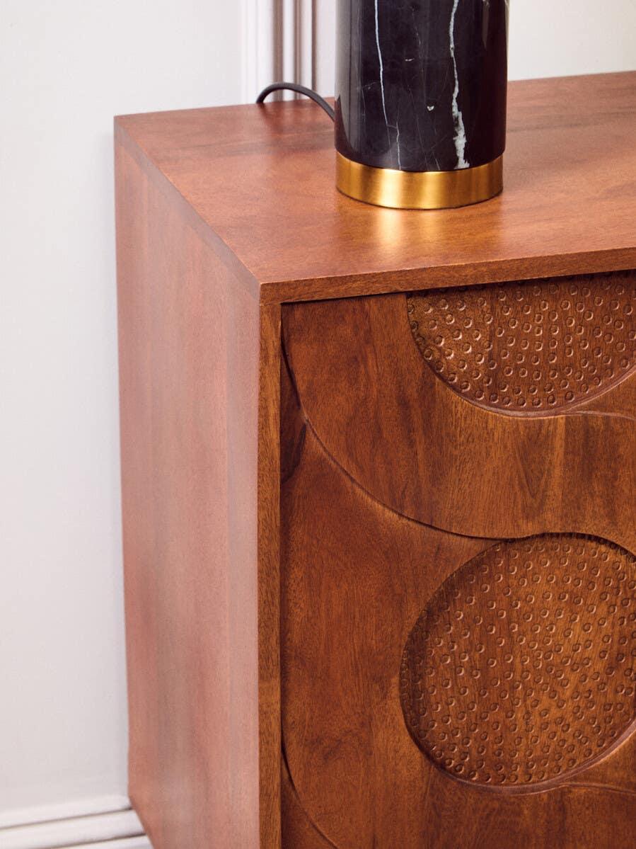 Wooden bedside table with carved geometric drawer detail and marble lamp