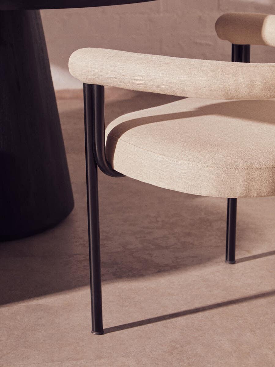 Beige upholstered dining chair with curved armrests and black metal legs