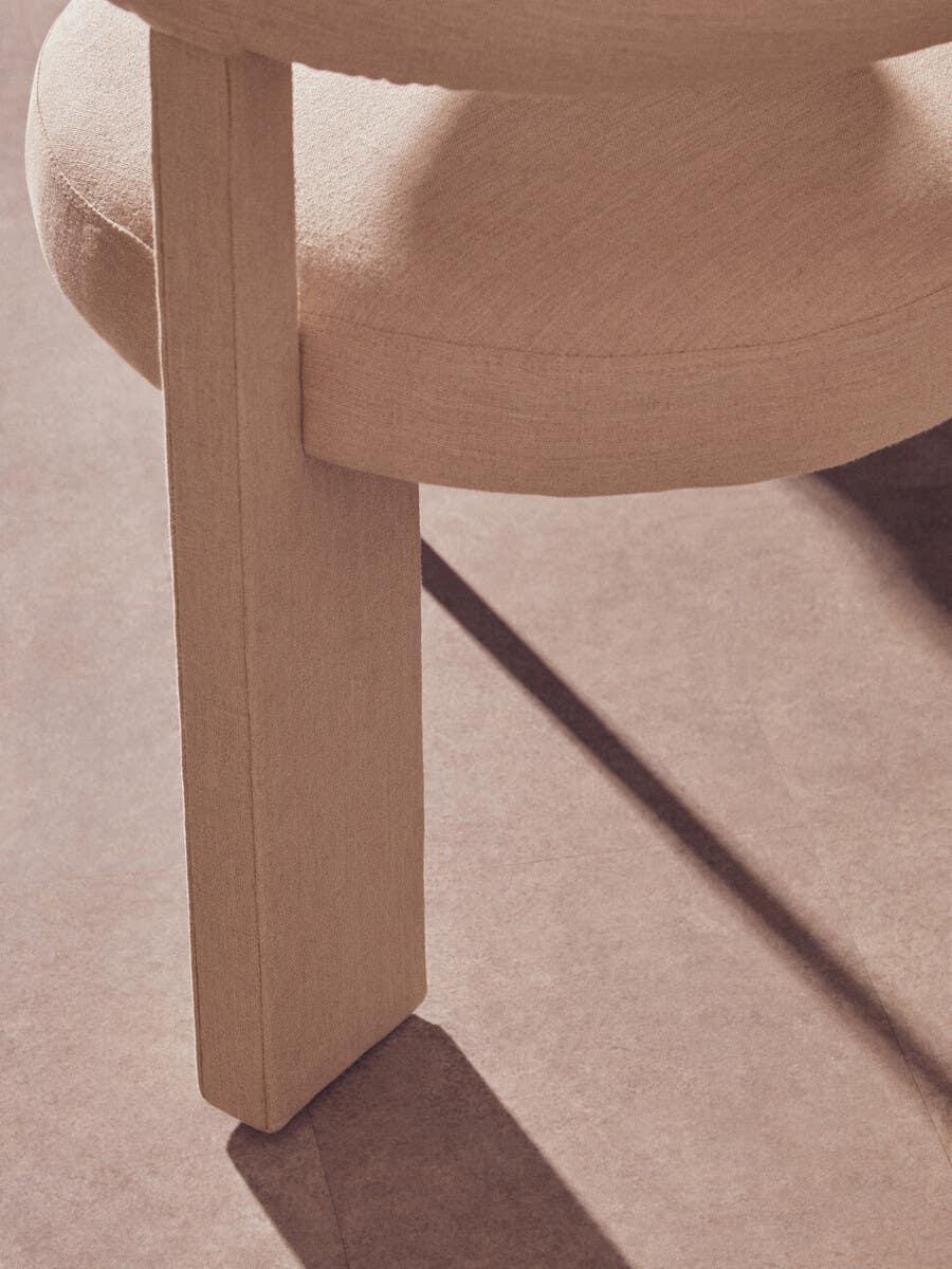 Close-up of beige upholstered dining chair leg and round seat on tiled floor