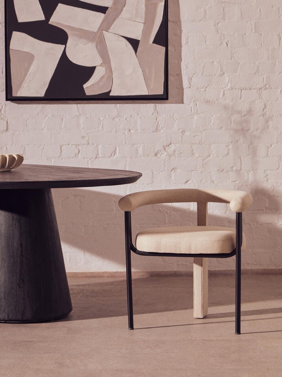Beige upholstered dining chair with black metal legs beside round dark dining table