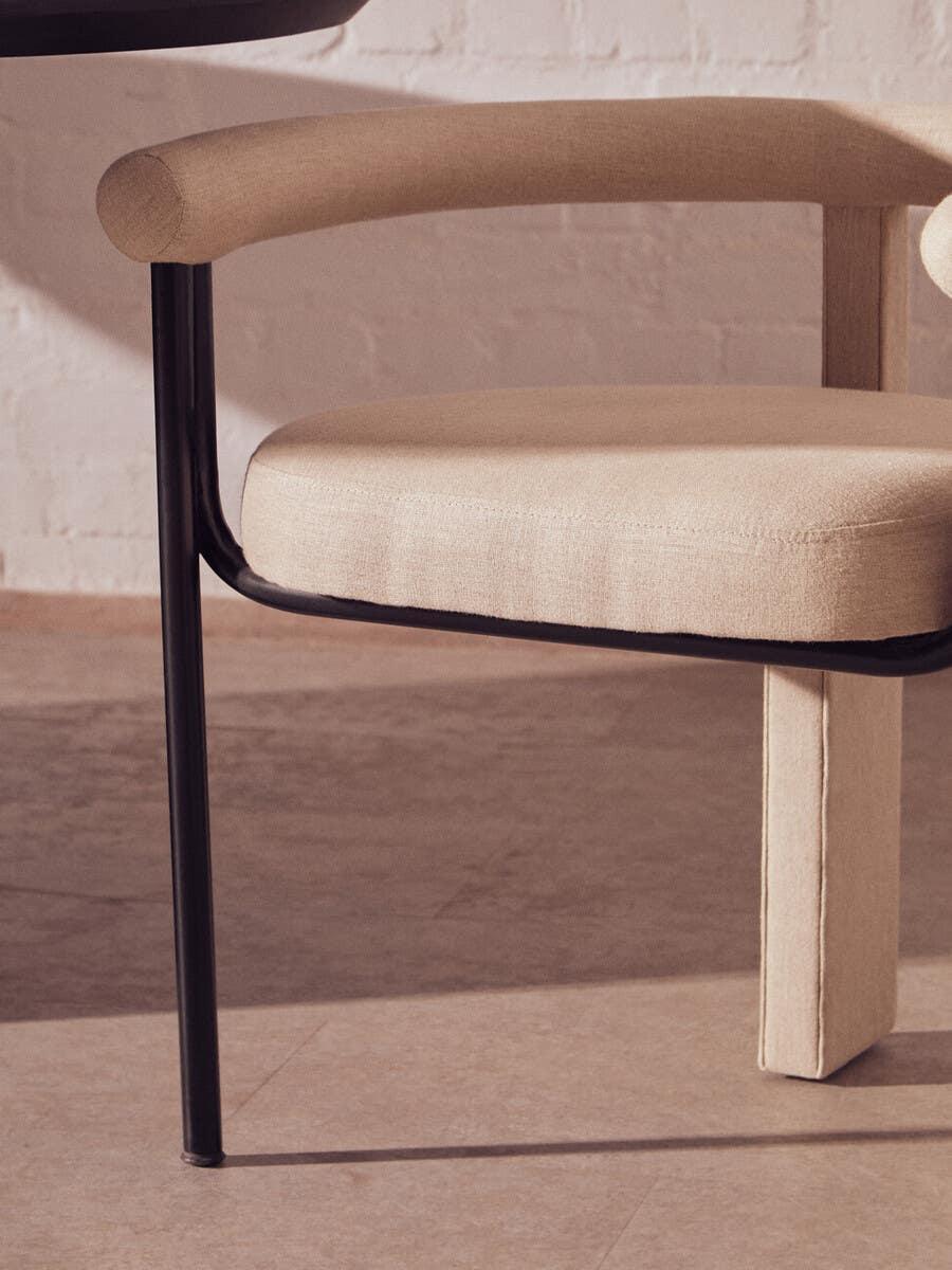 Beige fabric dining chair with padded seat, round backrest, and black metal leg