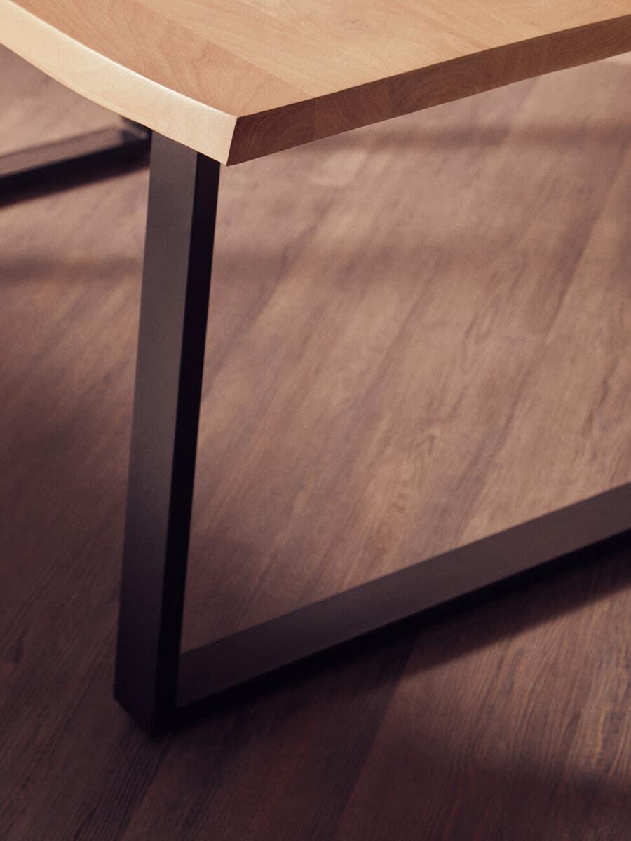 Dining table with light wood top and black metal legs on wooden floor