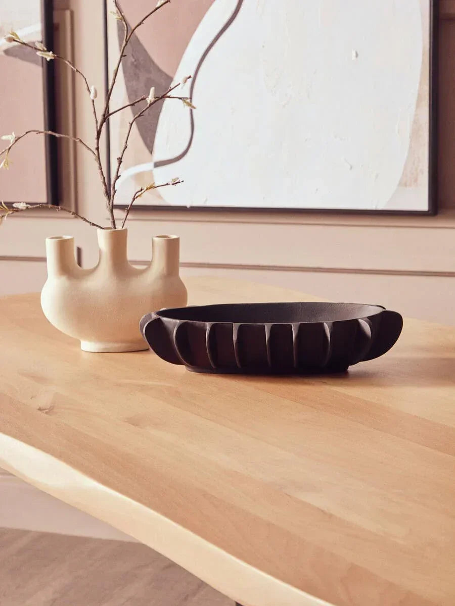 Modern wooden dining table with sculpted ceramic vase and black decorative bowl
