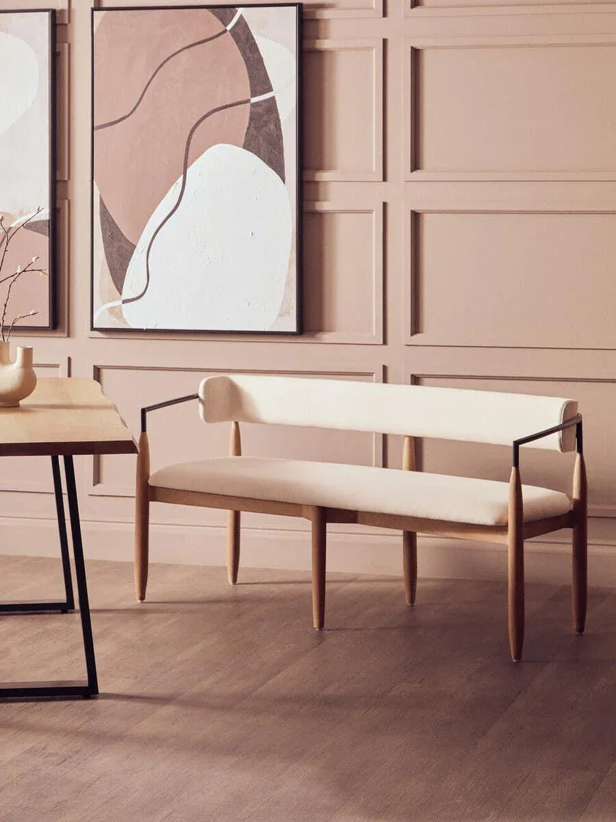 Cream upholstered bench with wooden legs and black metal arms beside modern dining table