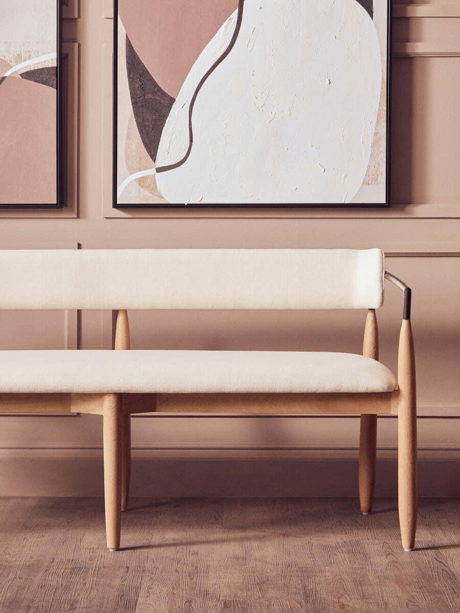 Modern cream upholstered bench with wooden legs in front of abstract wall art