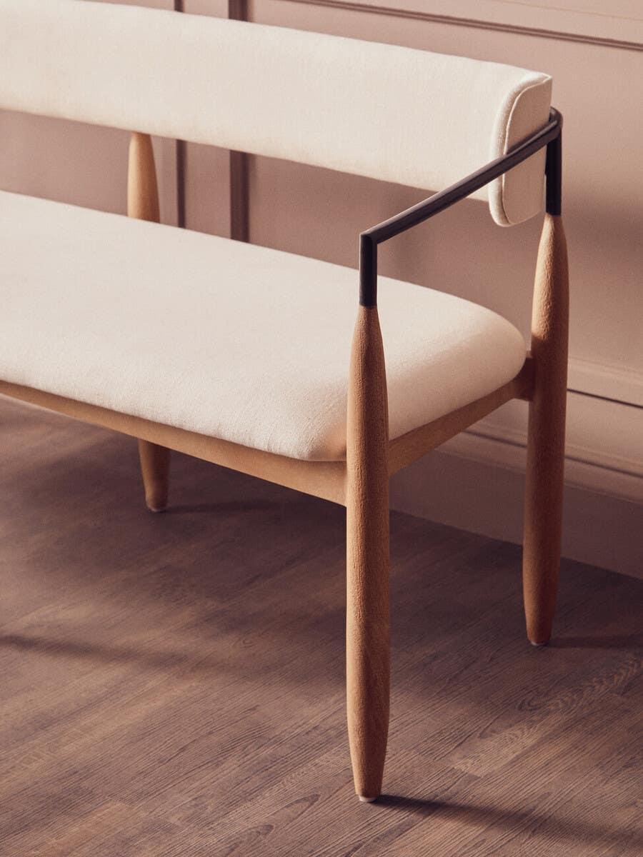Modern cream upholstered bench with wooden legs and black metal armrest detail