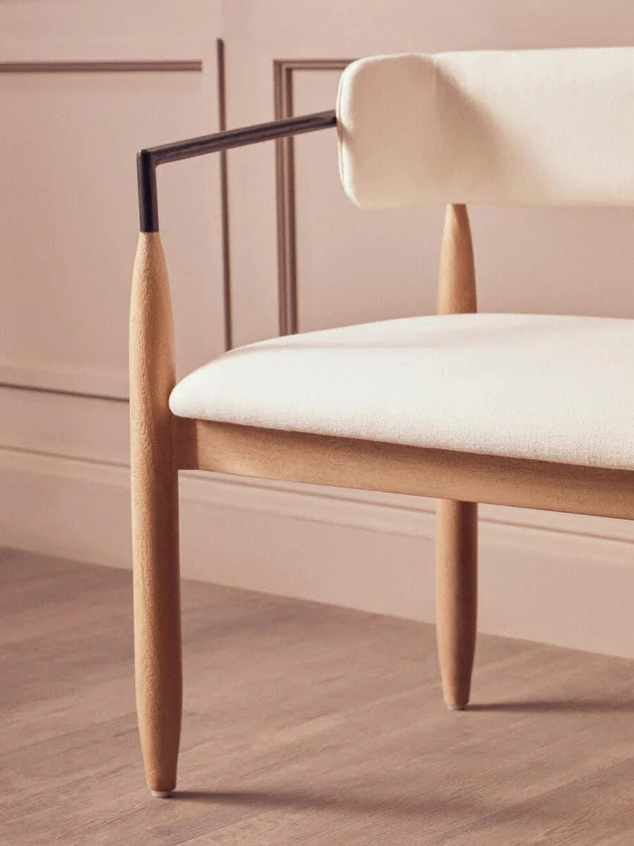 Modern cream upholstered armchair with wooden legs and metal detail on light wood floor