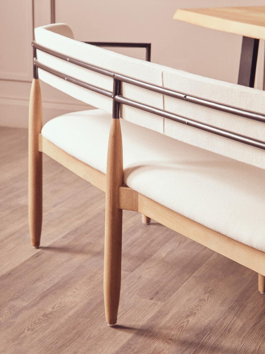 Modern dining bench with metal backrest, cream cushion, and light wood legs on wood floor