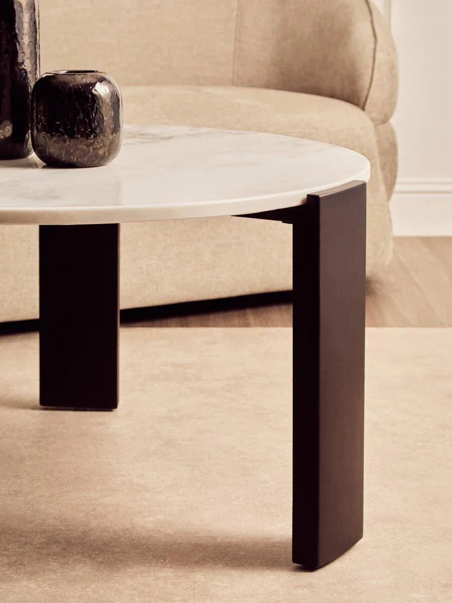 Round marble coffee table with black metal legs in front of beige fabric sofa