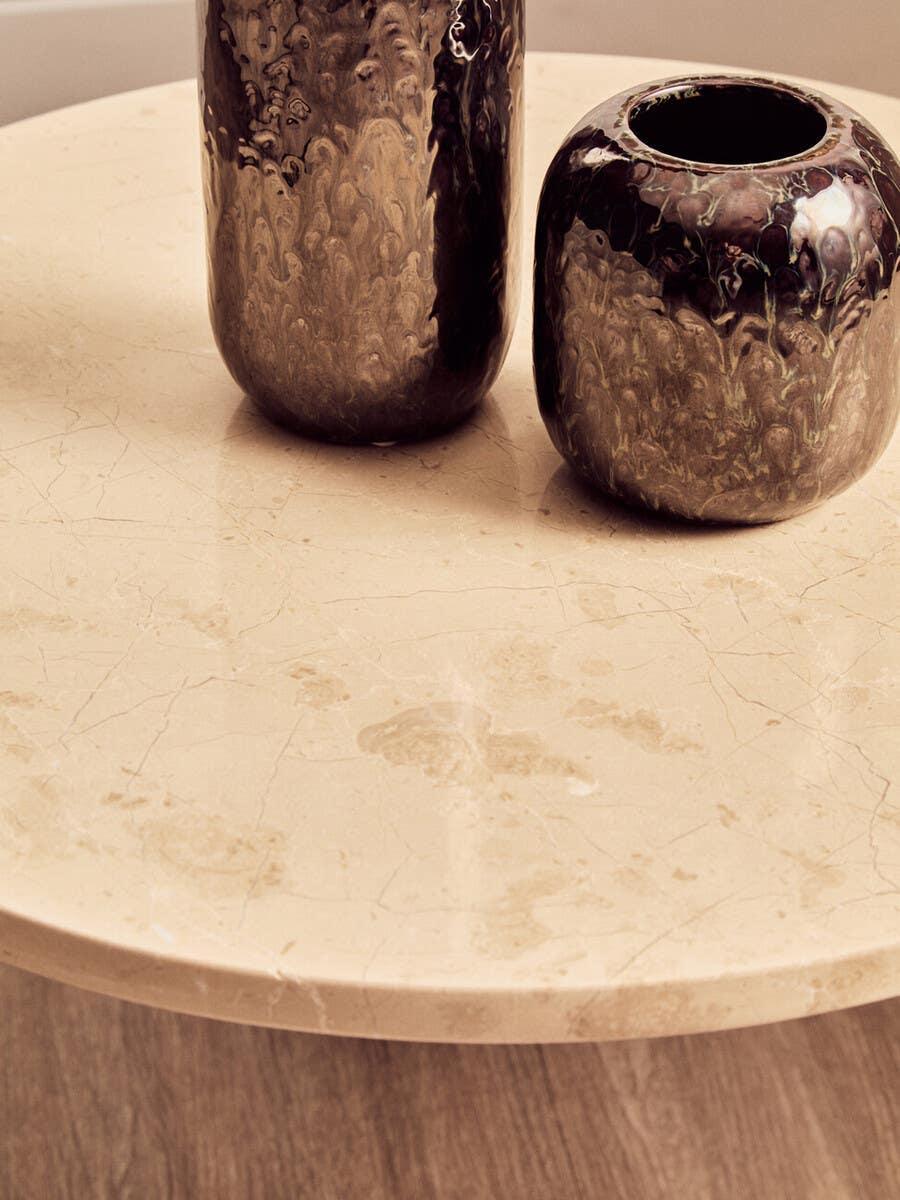 Round beige marble coffee table with two metallic vases on wood floor