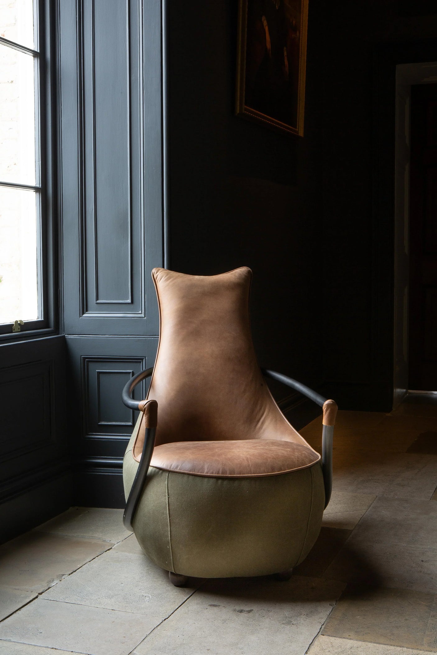 Brown leather accent chair with fabric base and curved arms in a dark room by a window