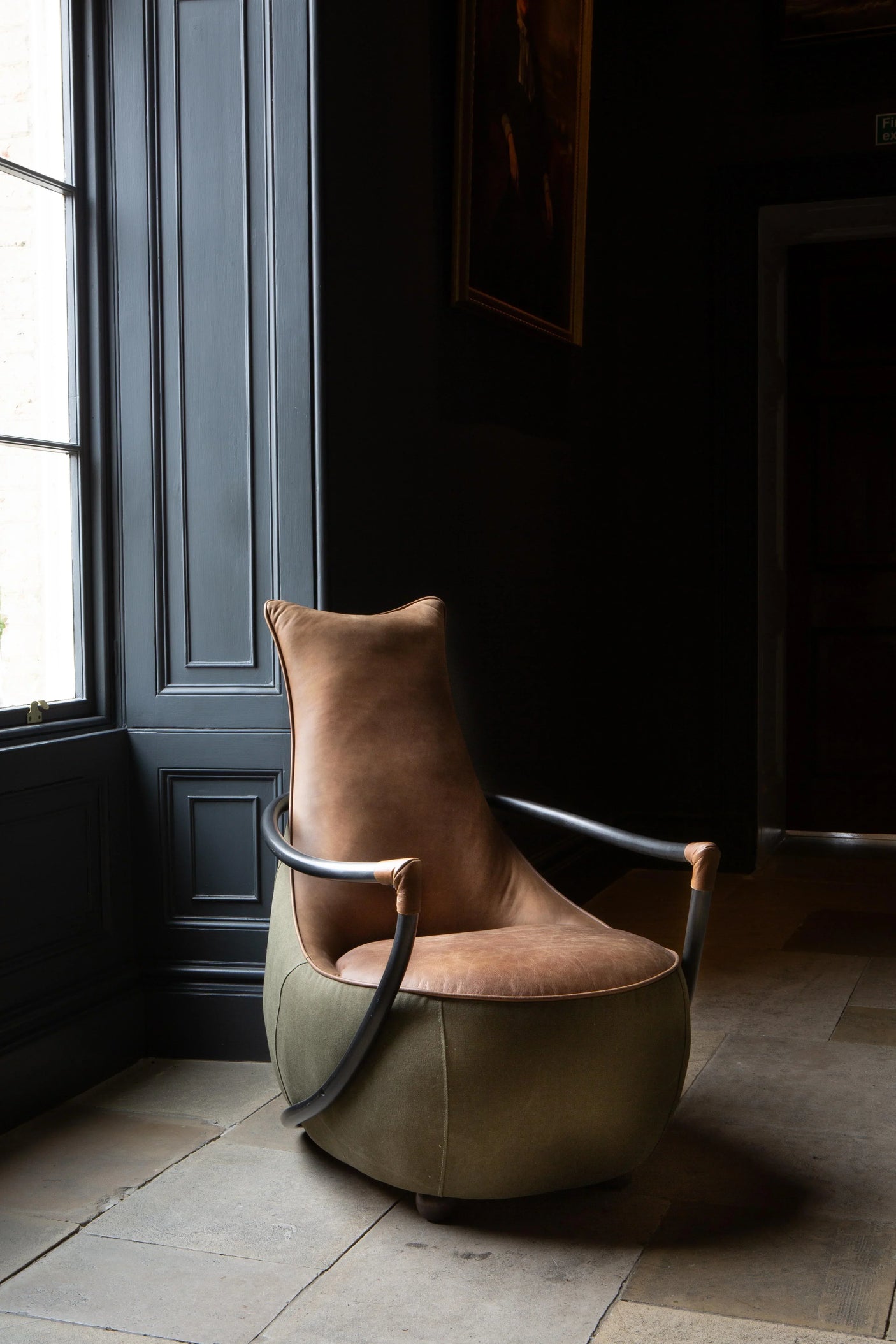 Brown leather accent chair with metal arms next to a window in a modern living room