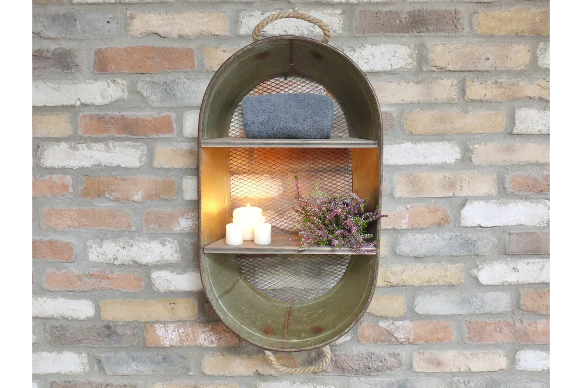 Oval metal wall shelf with rope handle holding candles, towel, and flowers against brick wall