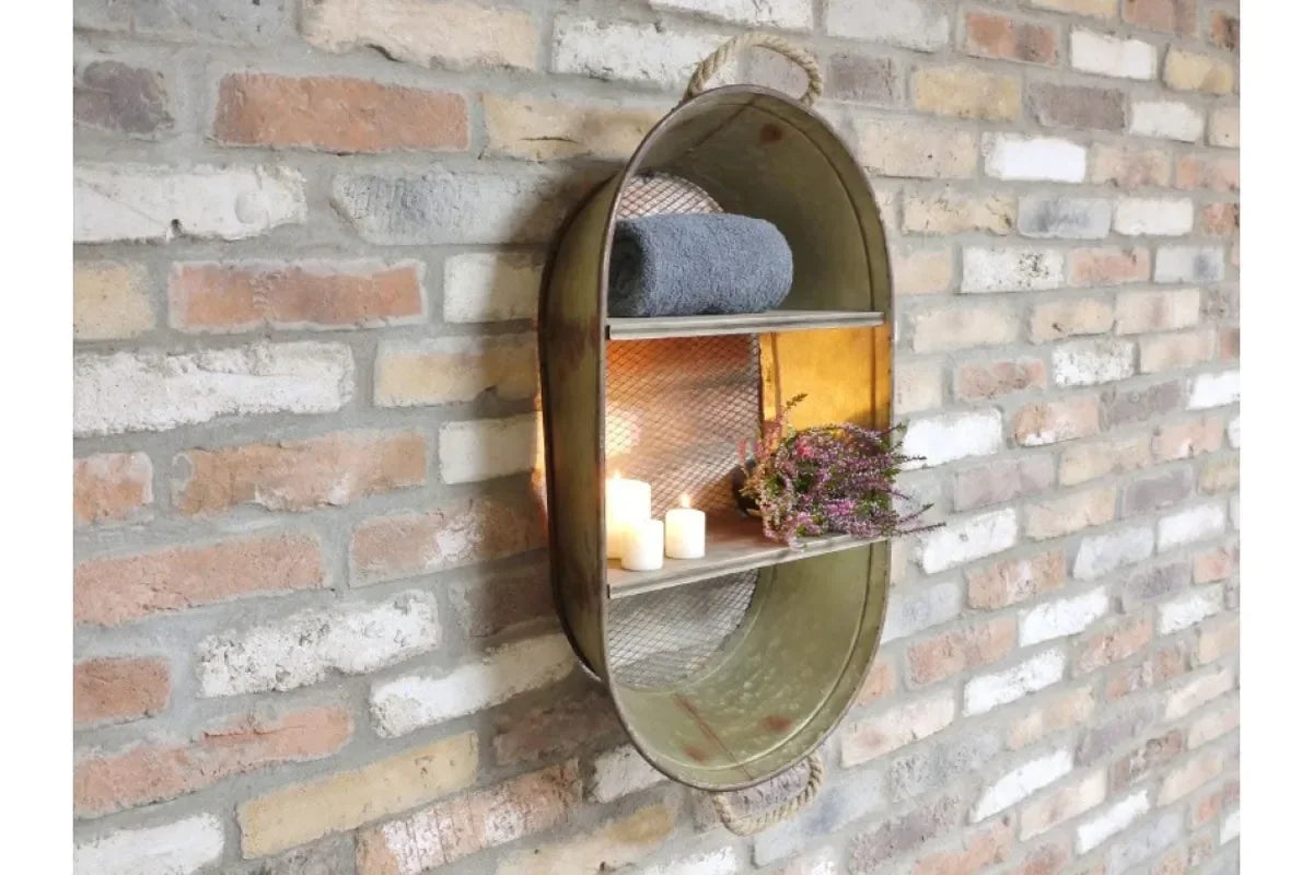 Oval metal wall shelf with mesh panels, displaying candles, towel, and flowers on brick wall