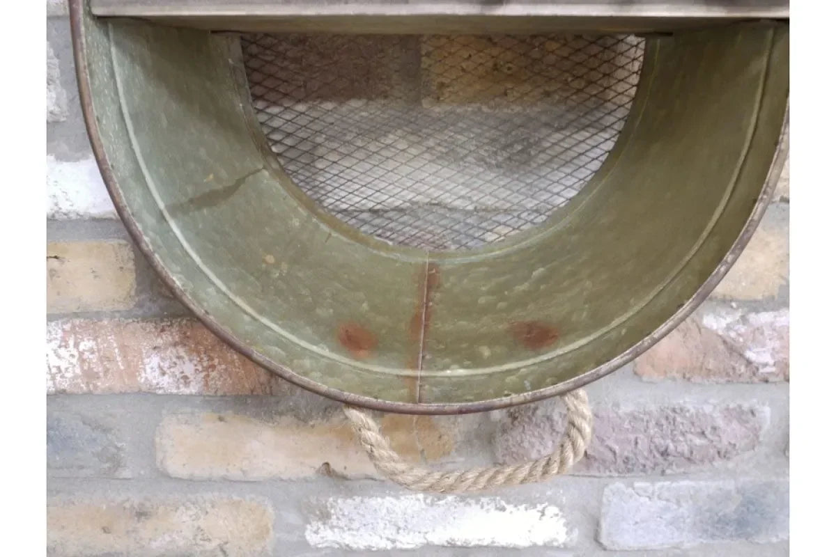 Round metal wall shelf with mesh backing and rope handle mounted on brick wall