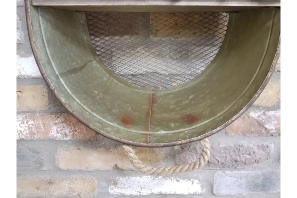 Vintage metal wall basket with rope handle and mesh back on brick wall