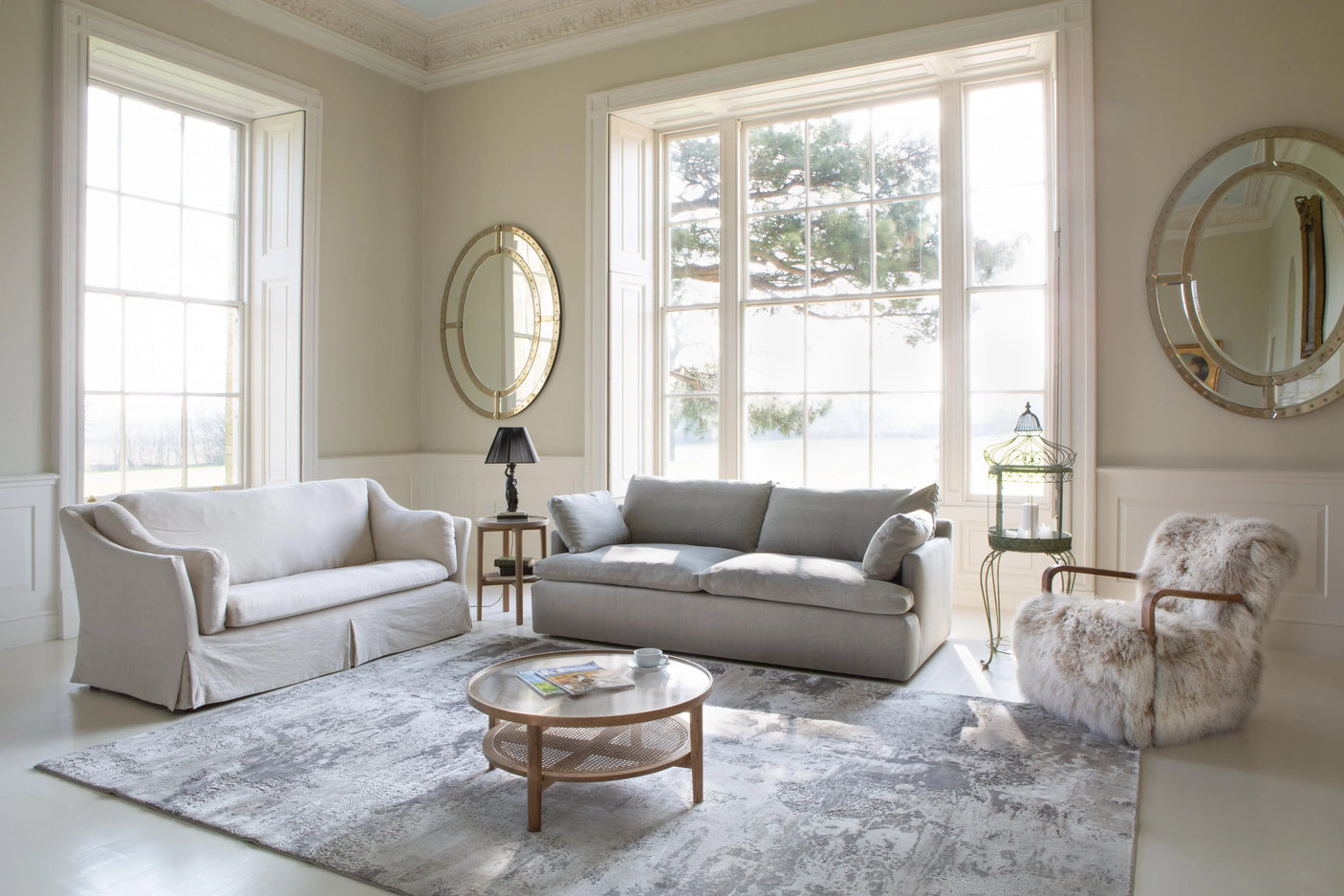 Light grey sofas and faux fur armchair in bright living room with large windows and mirrors