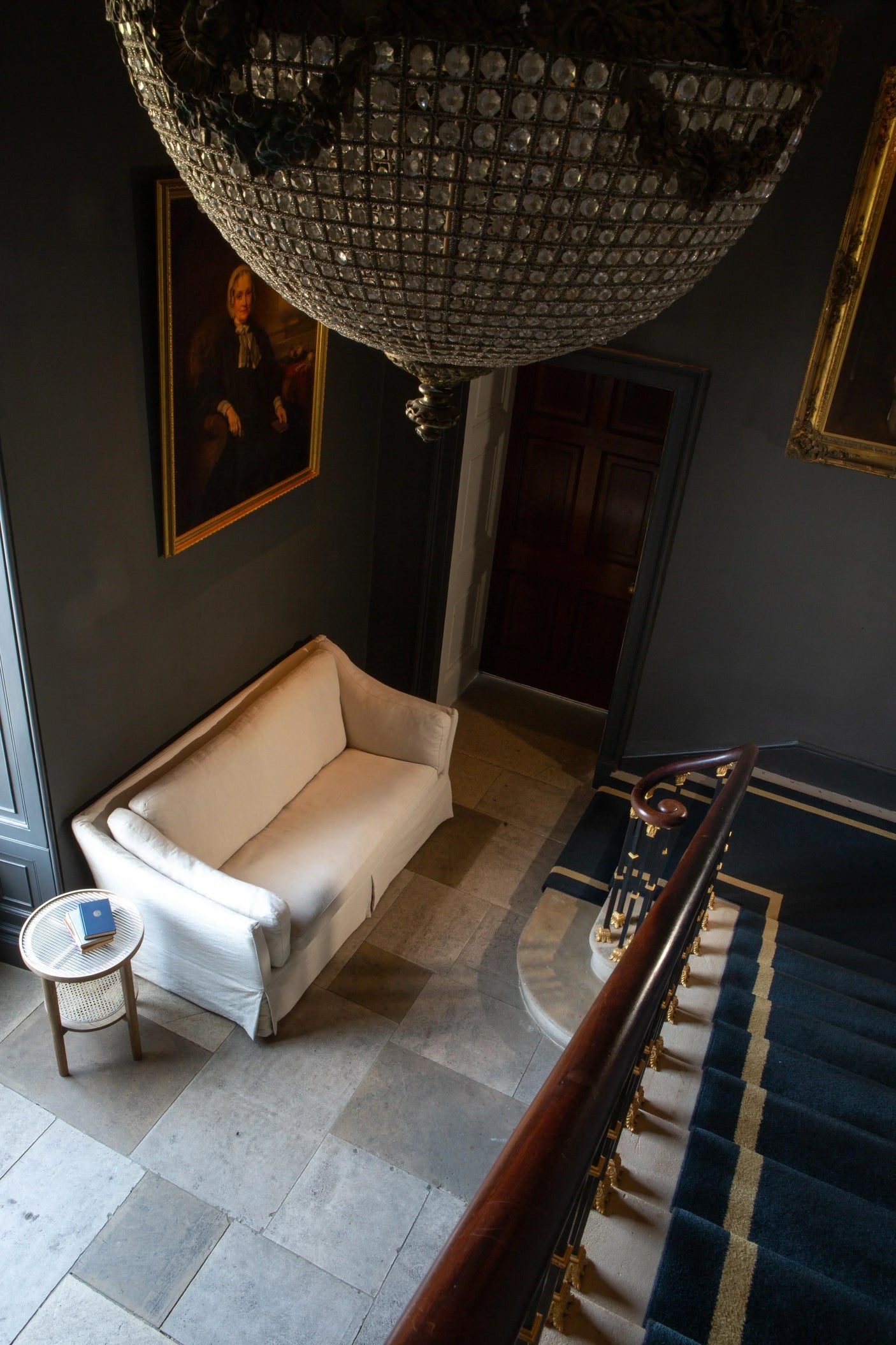 White fabric sofa beside round side table in hallway with stone floor and portrait on wall