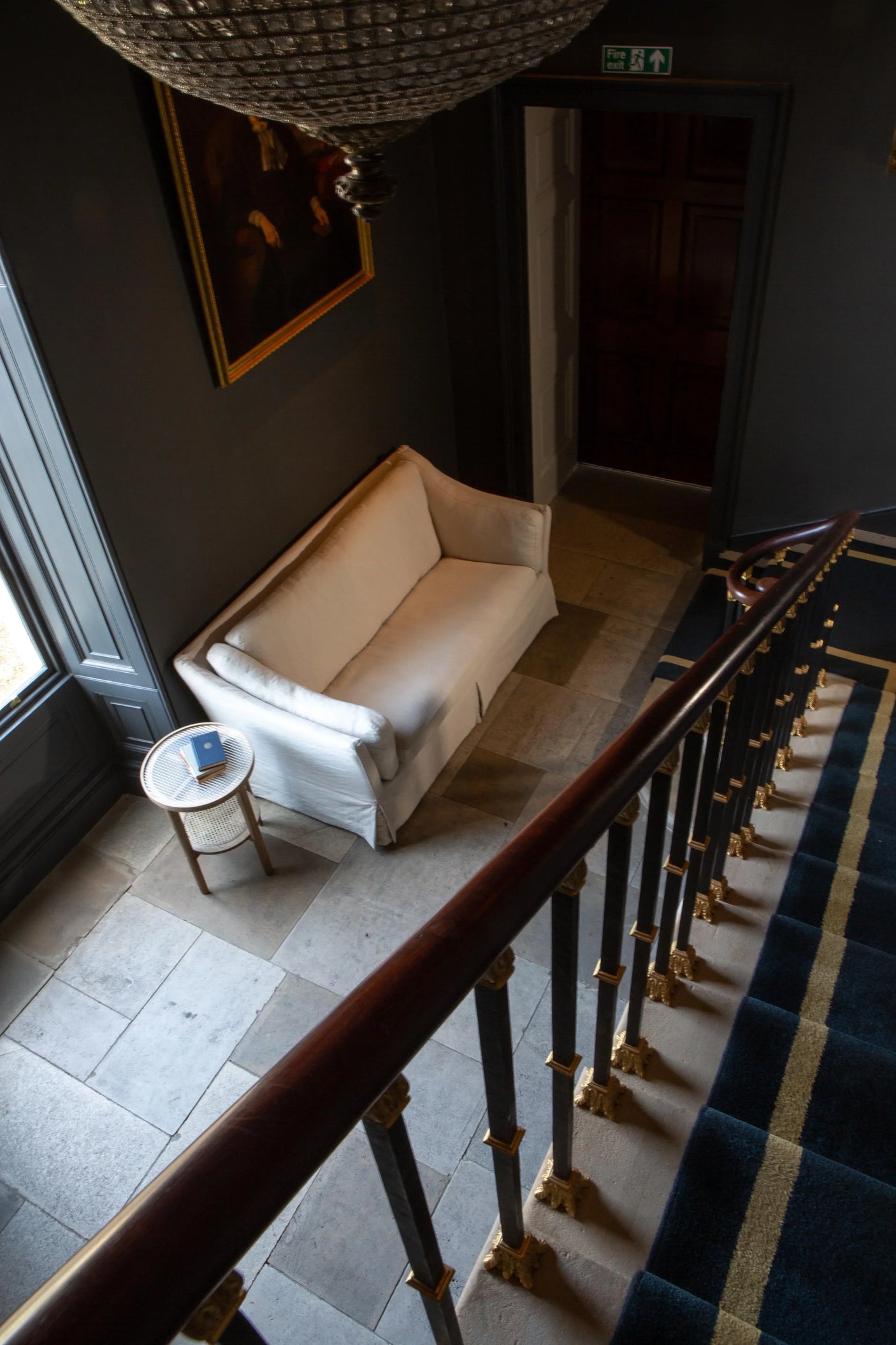 Cream fabric sofa with side table in hallway next to staircase and dark wall décor