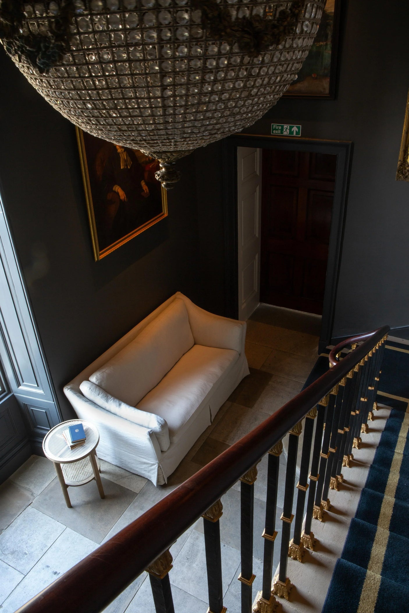 Cream fabric sofa in hallway beside round wooden side table and staircase with gold accents