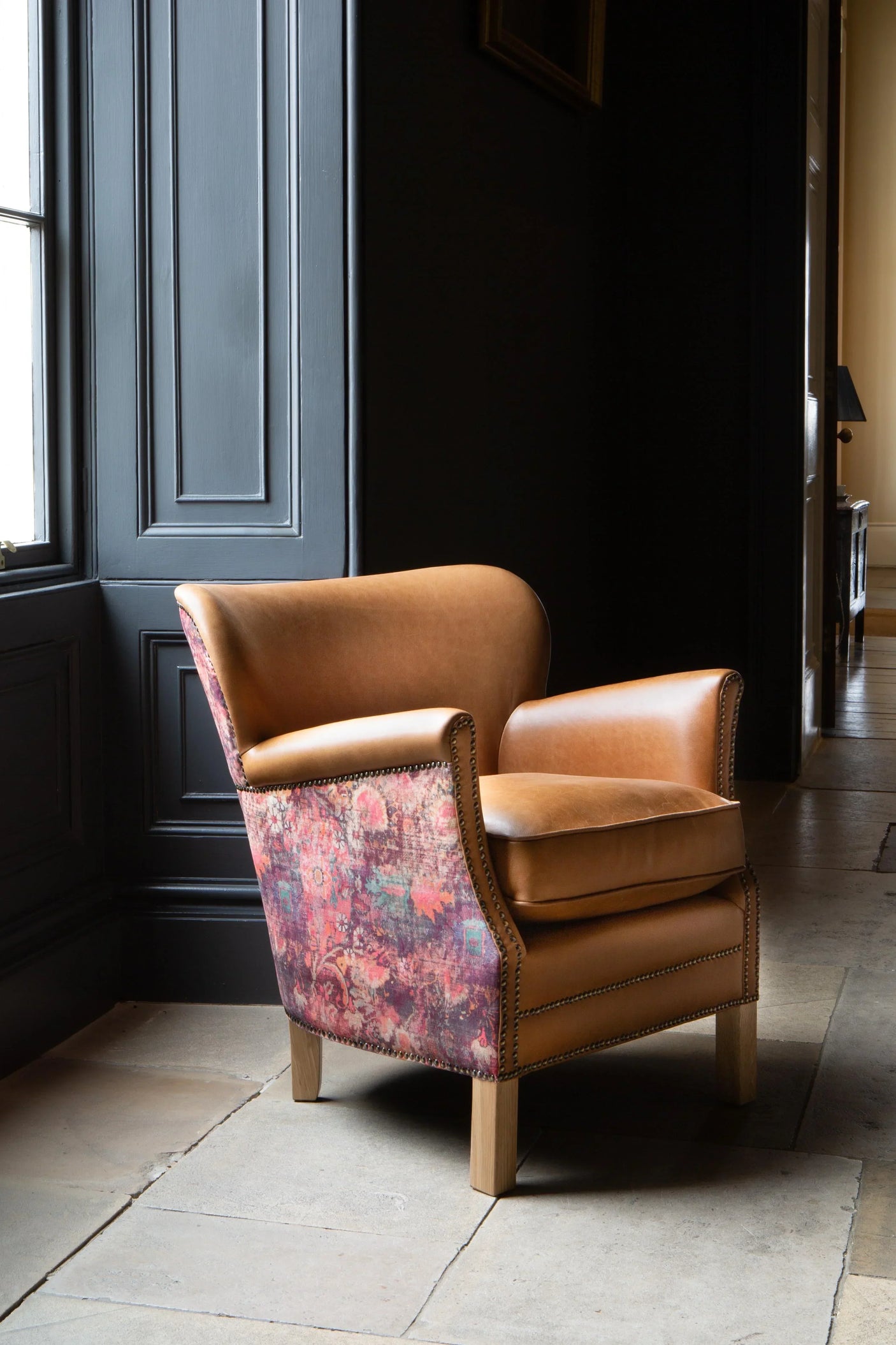 Tan leather armchair with patterned fabric sides and wooden legs in a modern interior