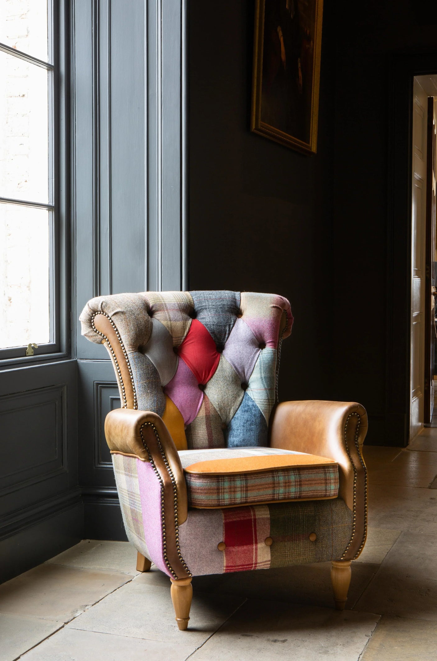 Patchwork armchair with leather arms and wooden legs by a window in a classic interior