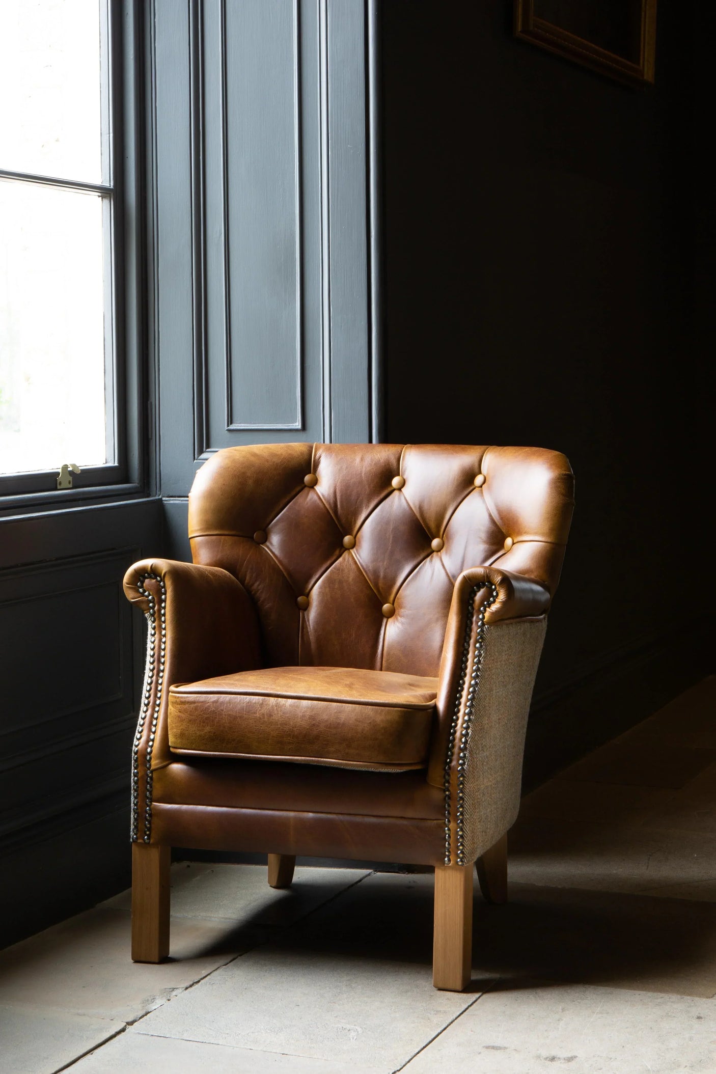 Brown leather armchair with button-tufted back and studded arms in natural light
