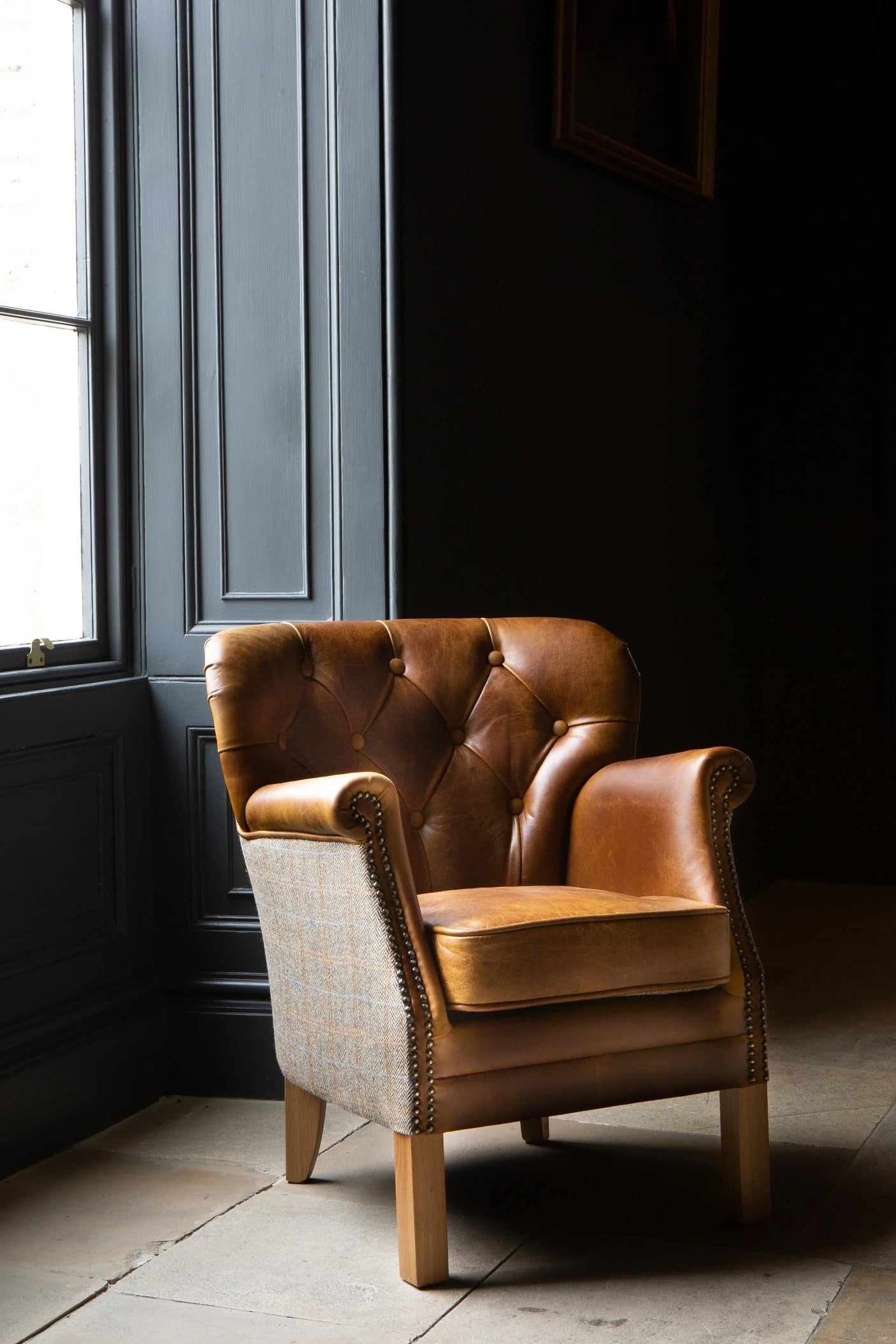 Brown leather armchair with button-tufted backrest and wooden legs near a window