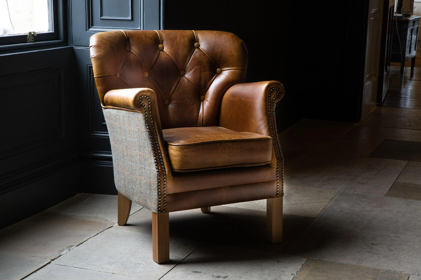 Brown leather armchair with tufted back and plaid fabric sides on wooden legs
