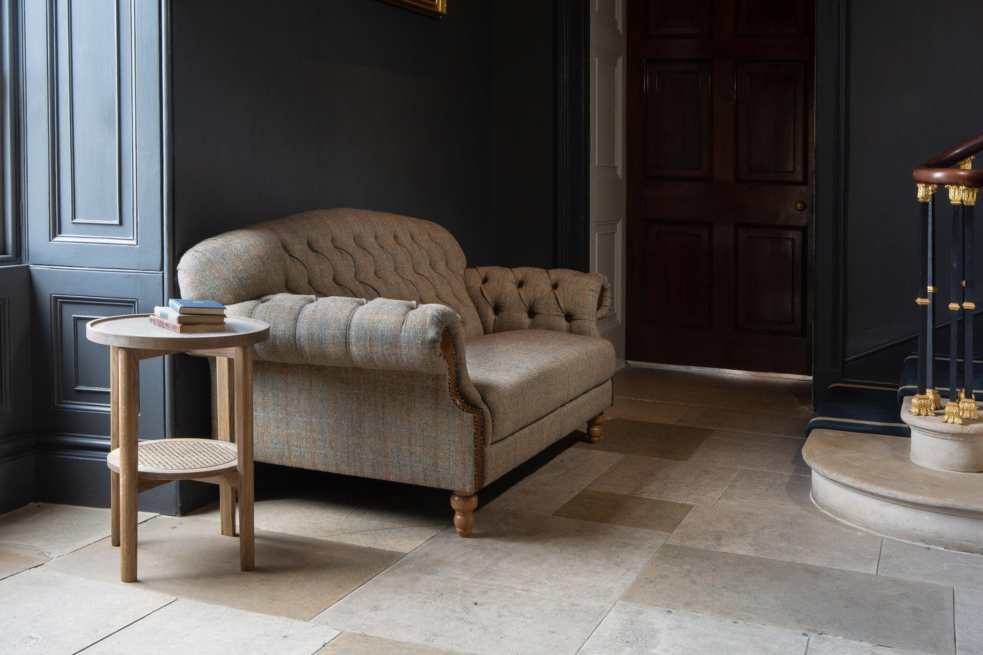 Plaid upholstered sofa with tufted back and wooden legs in a hallway next to a round side table