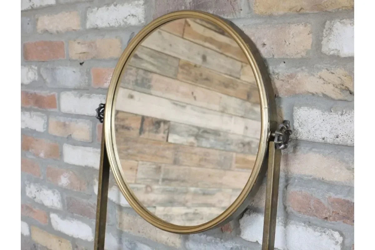 Round brass framed mirror with adjustable stand against rustic brick wall