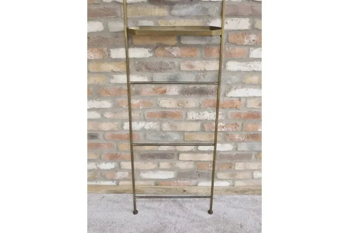 Brass metal blanket ladder with tray shelf against a brick wall on carpeted floor