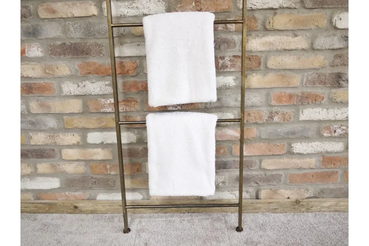 Brass towel ladder with two white towels against exposed brick wall